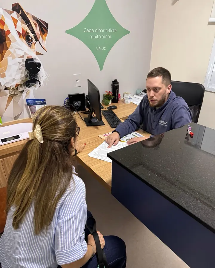Médico veterinário conversando com a tutora na mesa do consultório, antes do exame